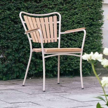 Mandalay Marguerit Outdoor Chair Teak Taupe in a garden setting with greenery and stone floor.